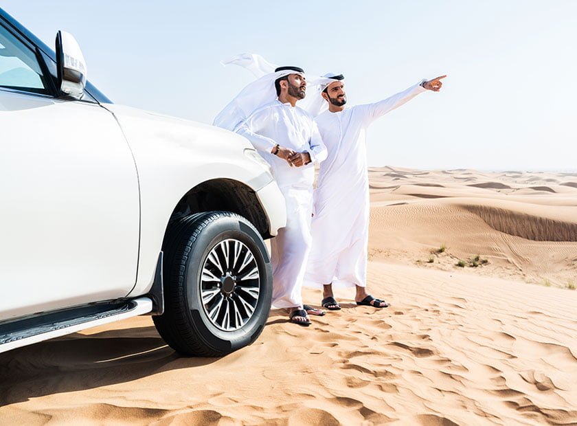 two men are talking in front of a car.